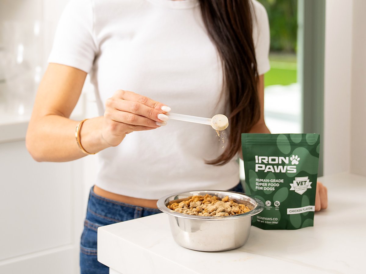Iron Paws superfood powder being scooped onto a bowl of dog food